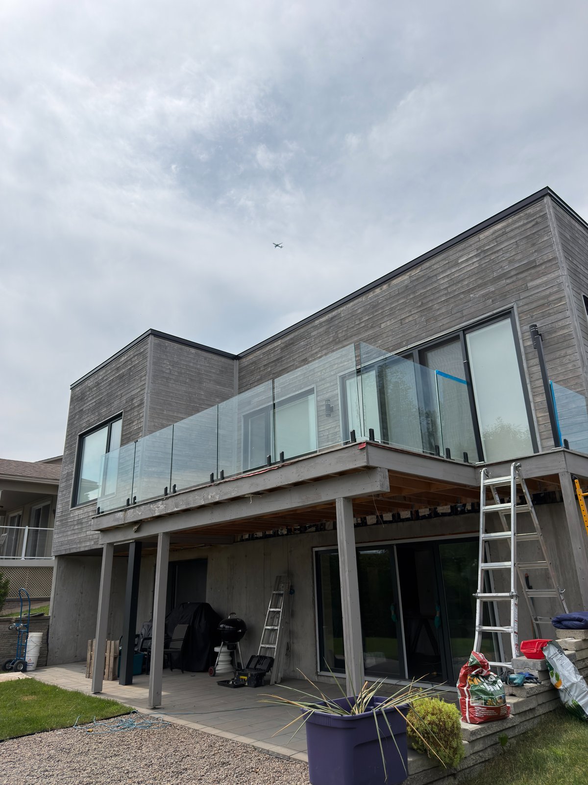 Rampe en verre trempé installée sur le balcon d'une maison moderne au revêtement de bois grisonné